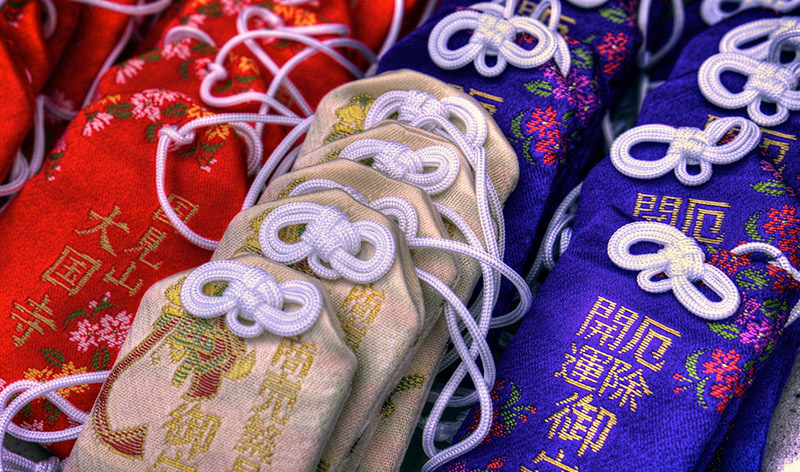 A photo of different omamori amulets for sale, each in gold, red, and purple varieties.